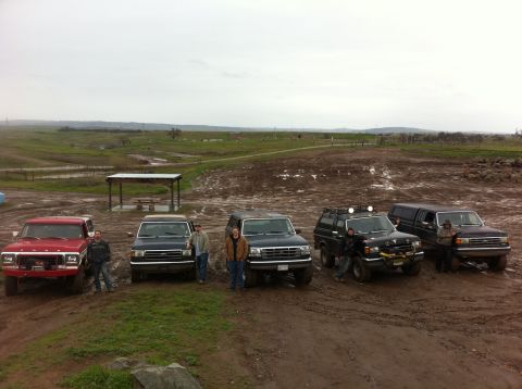 1990 Ford Bronco - Group of Ford Broncos and F-Series trucks parked in a muddy outdoor area.