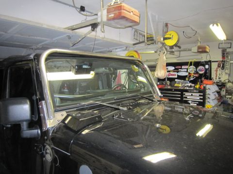 2008 Jeep Wrangler - Driver's-side view over the hood and windshield of a black Jeep Wrangler parked in a home garage, showing bare stainless/aluminum cowl brac…