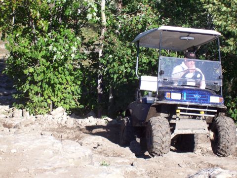 1978 Ford F-150 - A person drives a modified golf cart with off-road tires through a rough, wooded terrain.