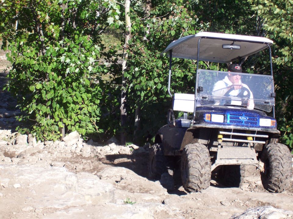 Golf cart with big tires driving on a rocky trail with trees around