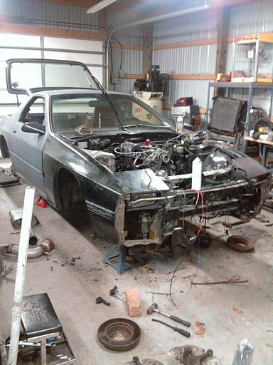1987 Mazda RX-7 - This 1987 Mazda RX-7 is undergoing repairs in a garage, with its hood open and engine visible.