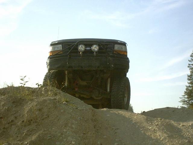 Lifted black Ford truck with grille guard and driving lights cresting a dirt mound head-on