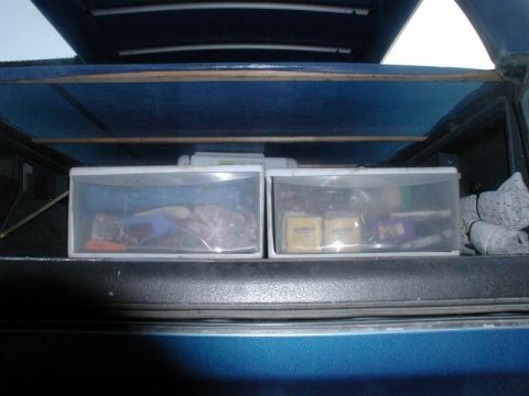 1985 Ford Bronco - The interior of a blue vehicle's cargo area shows two storage bins and rolled up fabric on the right side.