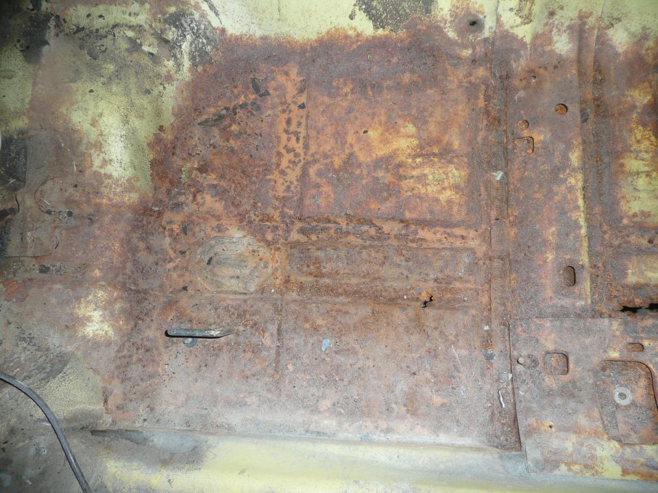 heavily rusted floor pan with yellow undercoating visible