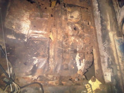 1973 Ford Ranchero - The floor pan of a vehicle shows extensive rust and damage, obscuring any specific year or model identification.