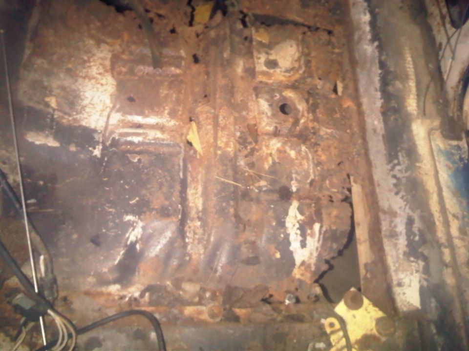 Heavily rusted vehicle floor pan with exposed metal and wiring