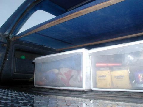 1985 Ford Bronco - The interior cargo area of a vehicle contains plastic storage bins and yellow boxes with "precision" labels.