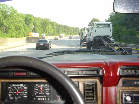 1986 Ford Bronco - Interior view of a vehicle on the highway, showing a car carrier truck transporting other vehicles.
