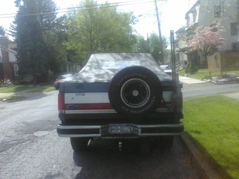 Rear view of a 1987 Ford Bronco with a soft top and spare tire mounted on the back. The license plate reads HHB-0022