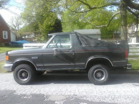 1988 Ford Bronco - Side view of a dark gray 1988 Ford Bronco a black soft top cover.