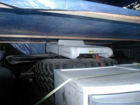 1985 Ford Bronco - The interior cargo area of a vehicle is filled with a spare tire, storage bins, and covered by tarps.