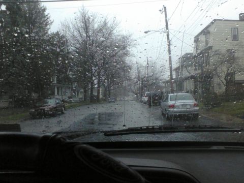 1988 Ford Bronco - Raindrops on the windshield obscure the view of a residential street on an overcast day.