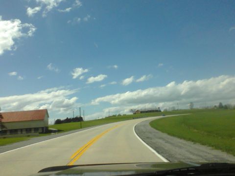 1988 Ford Bronco - View from inside a vehicle driving on a country road, passing a barn and rolling hills under a partly cloudy sky.