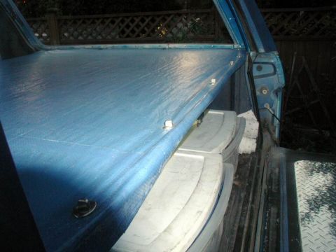 1985 Ford Bronco - The interior cargo area of a vehicle is covered by a blue tarp, with storage bins visible beneath.