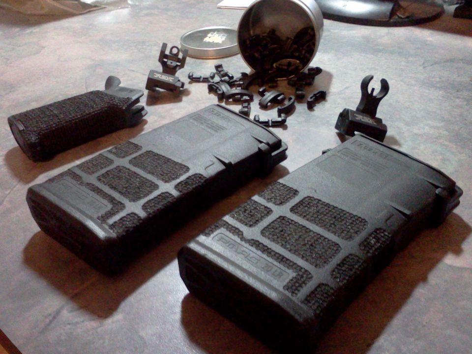 Two AR-15 magazines, a pistol grip, and several iron sights are laid out on a table