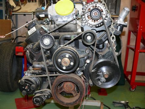 1976 Chevrolet Corvette - Engine assembly with various components and belts, suspended by a chain.