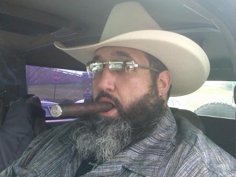 1993 Ford Bronco - A man wearing a cowboy hat and glasses smokes a cigar while inside a vehicle.