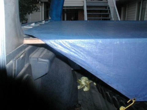 1985 Ford Bronco - The interior of a vehicle's cargo space is partially covered by a blue tarp, with visible straps and a seatbelt.