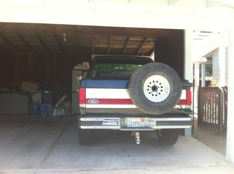1990 Ford Bronco - A Ford pickup truck is parked in a garage, showing its rear end and spare tire.