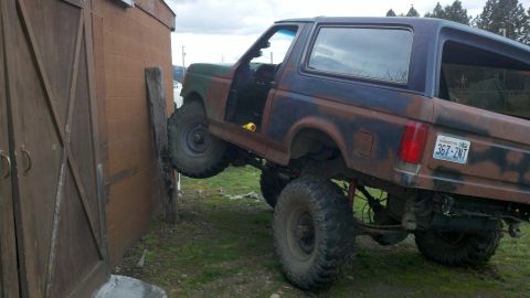 1988 Ford Bronco - This 1988 Ford Bronco, painted in camouflage, has its driver's door open and is leaning against a wooden shed.
