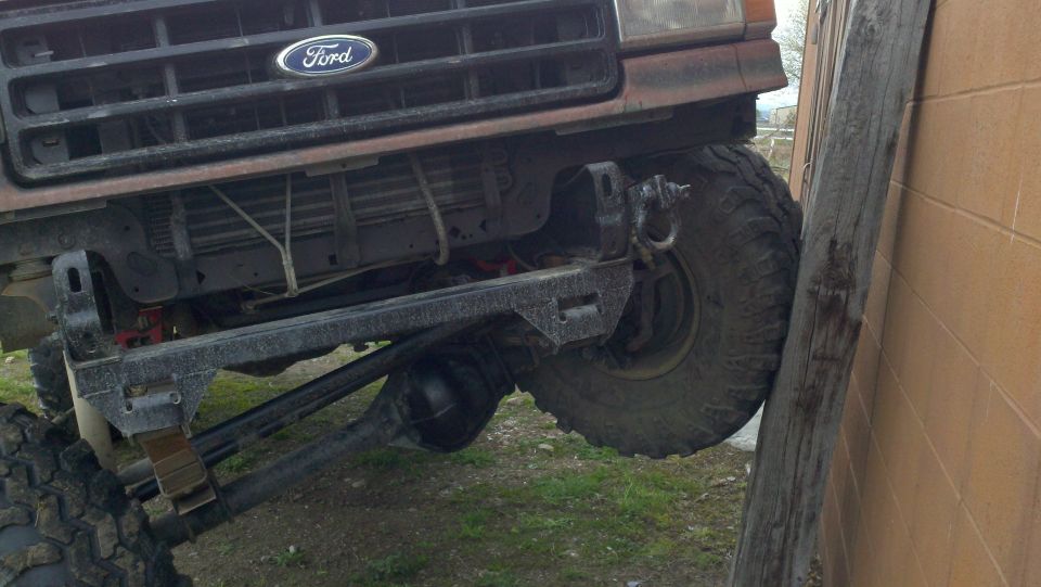 Front underside of a lifted Ford 4x4 flexed against a block wall showing axle and leaf springs