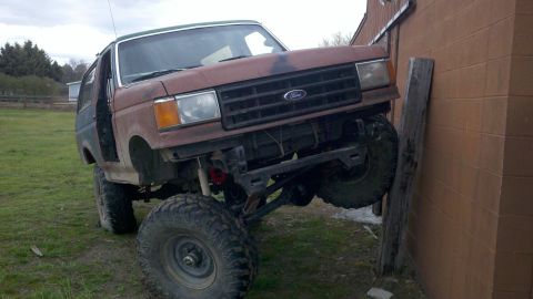 1988 Ford Bronco - This modified Ford Bronco is positioned with its front tire resting on a wooden post against a brick wall.