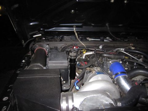 2008 Jeep Wrangler - Night-time engine bay shot showing a supercharger or forced-induction install, with a polished aluminum intake housing, blue silicone coupl…