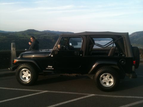 2005 Jeep Wrangler - A black 2005 Jeep Wrangler Unlimited is parked outdoors with a scenic view of hills and water in the background.