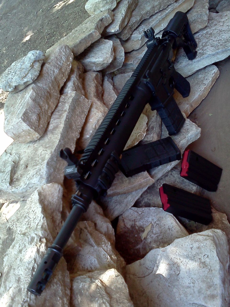 Assault rifle with three magazines, two with red followers, resting on rocks