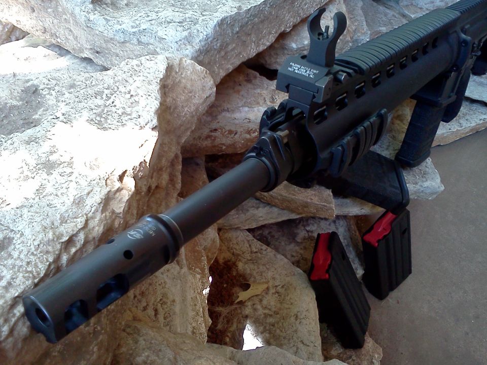 Close-up of an assault rifle with two magazines, one with a red follower, resting on rocks
