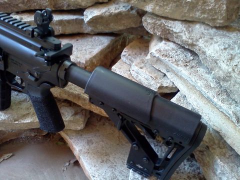 1996 Ford Bronco - Close-up of an assault rifle's stock and receiver, set against a textured stone background.