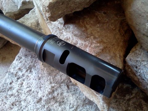 1996 Ford Bronco - A close-up view of a black muzzle brake with visible text and cutouts, positioned against a rocky background.