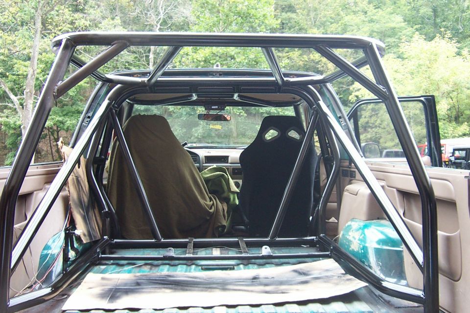 Black multi-point roll cage built into a gutted SUV interior, viewed from the rear hatch