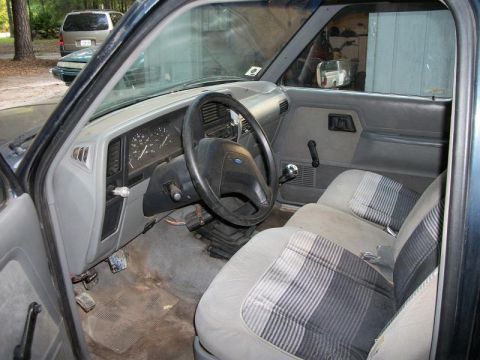 1994 Ford Explorer - The interior of a dark blue pickup truck, plaid seats and a dashboard that appears to be from 1994. Other vehicles are visible through the…