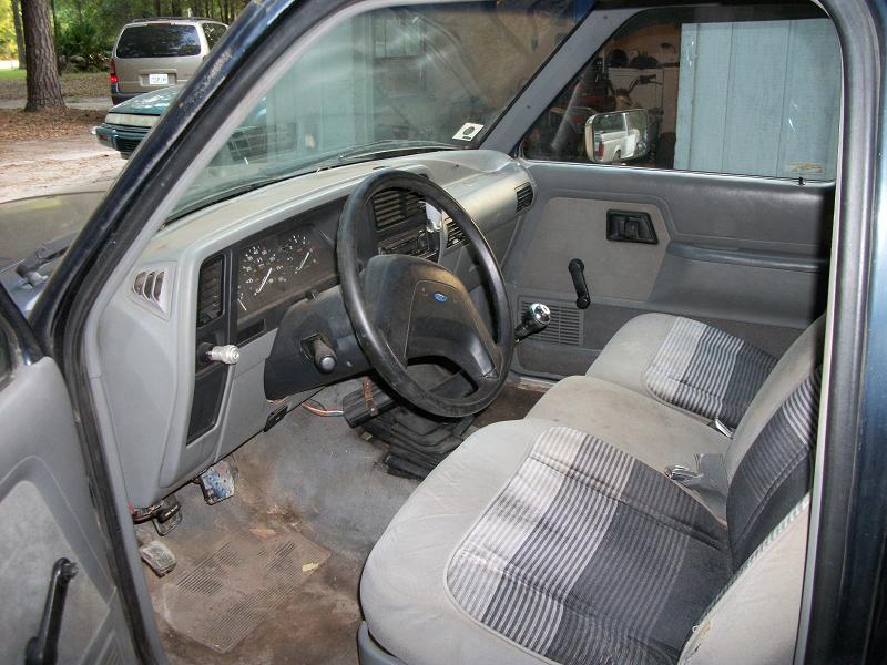 Interior of a dark blue pickup truck with plaid seats and a 1994 dashboard. Two other vehicles are visible outside