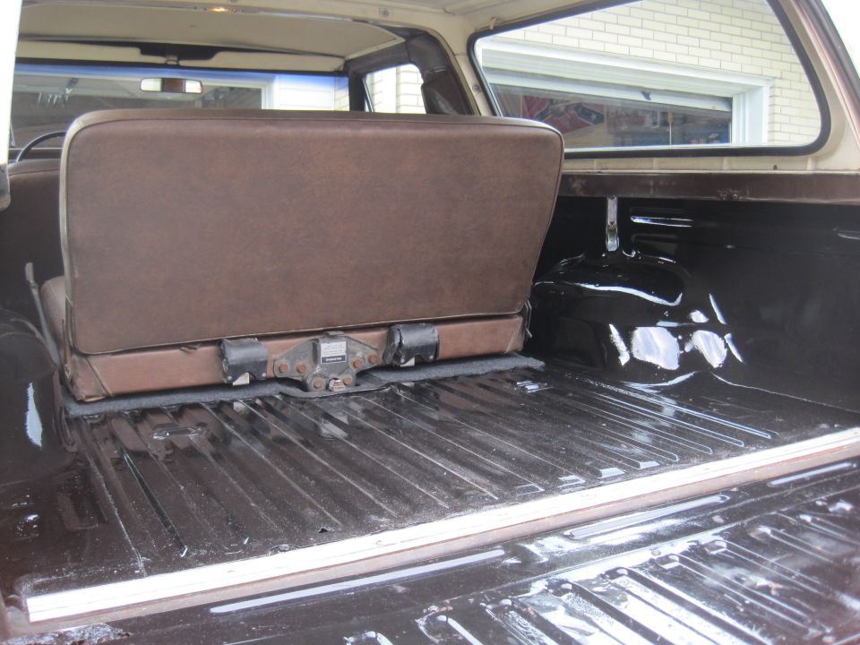 Brown vinyl seat folded up in dark cargo area of an SUV. Ribbed floor, white trim. Watermark 'SUPERMOTORS.NET'