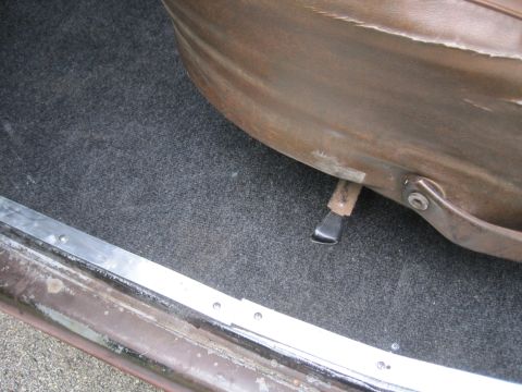 1979 Ford Bronco - Close-up of a car's interior, focusing on the carpet and seat base with a visible lever.