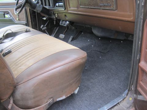1979 Ford Bronco - The interior of the vehicle features a two-tone seat, a steering wheel, and a dark carpeted floor.