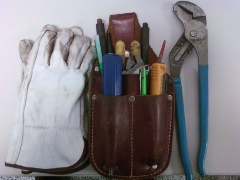 1989 Ford Bronco - A pair of work gloves rests beside a leather tool belt holding various tools and writing instruments.