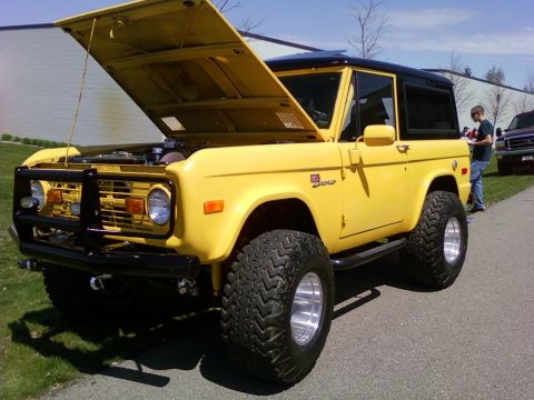 1989 Ford Bronco - A bright yellow Ford Bronco sits with its hood open, revealing the engine bay. A person stands nearby.