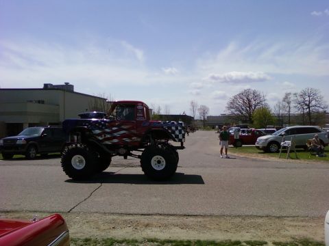 1989 Ford Bronco - A custom monster truck with a patriotic paint scheme is parked outdoors, with other vehicles and buildings in the background.