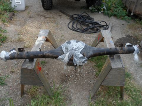 1991 Ford Bronco - A differential axle, taped and secured on sawhorses, sits on a dirt ground with a black hose nearby.