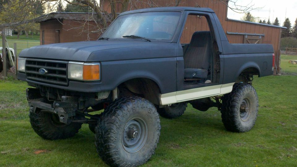 Dark blue Ford Bronco with lifted suspension and large tires, driver's door removed