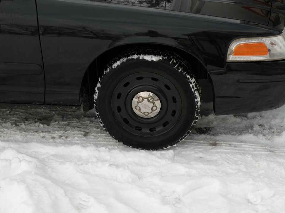 Black sedan's front wheel and fender covered in snow. Orange turn signal visible