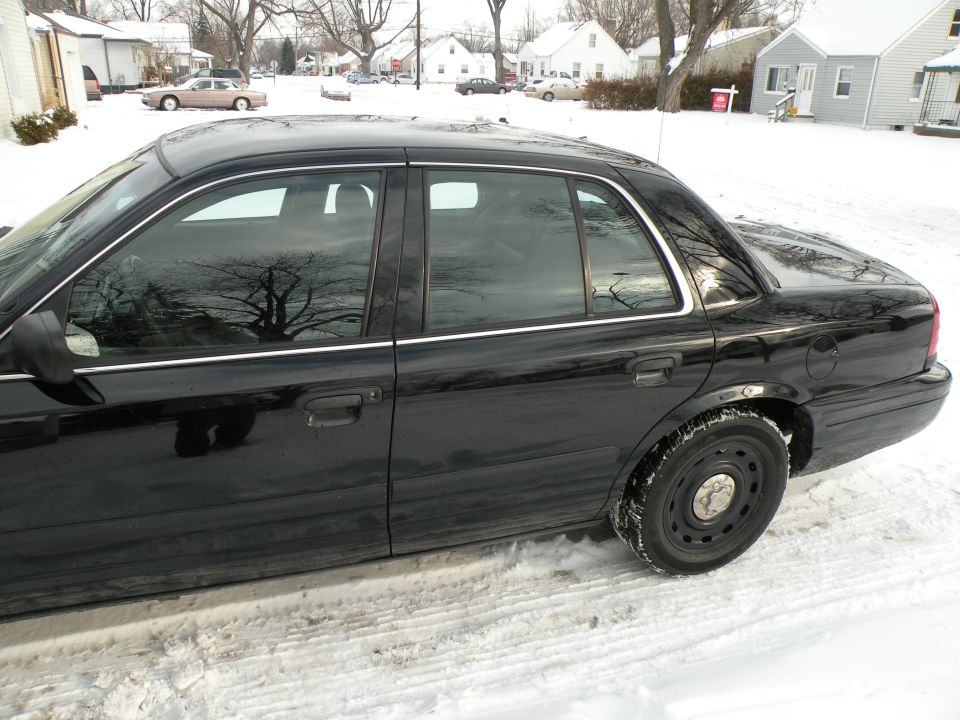 Black sedan parked on a snowy street. Side view shows the doors, windows, and rear wheel
