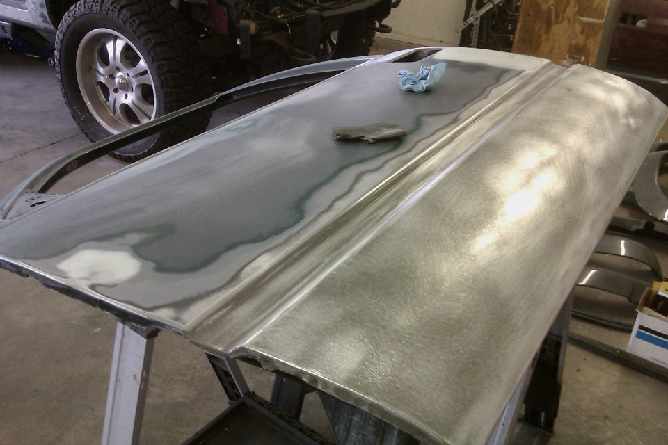 Car door stripped to metal, being prepped for paint. Another vehicle's tire is visible in the background