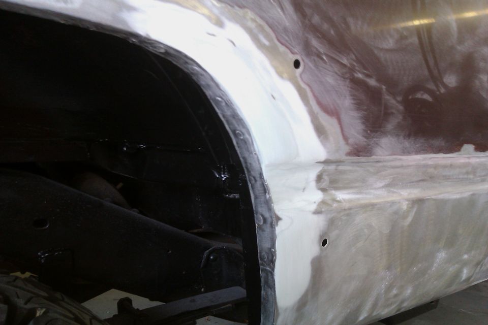 Close-up of a vehicle's rear wheel well with body filler and primer on the fender