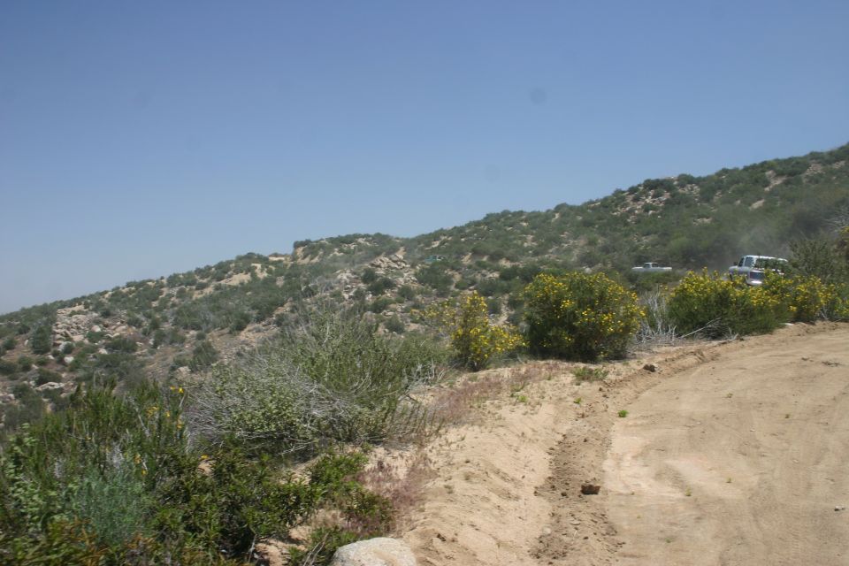 Two SUVs drive on a dirt road through a dry, hilly landscape with sparse vegetation