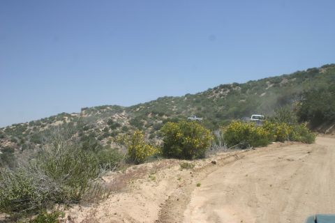 1991 Ford Bronco - Two vehicles navigate a dusty trail through a dry, brush-covered hillside under a clear blue sky.