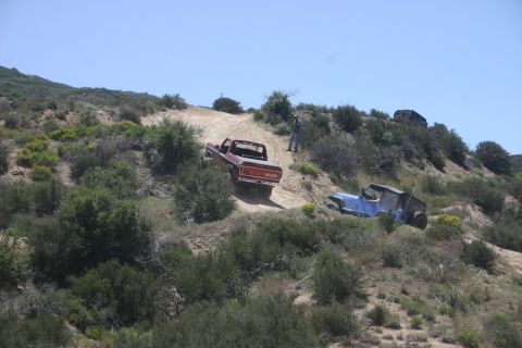 1991 Ford Bronco - A red 1979 Ford F-150 pickup truck navigates a steep dirt trail, with a blue Jeep and another vehicle visible in the distance.